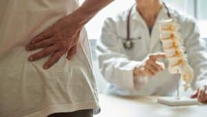 A male doctor explaining herniated disc treatment to female patient complaining of back pain at medical clinic