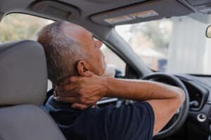 Middle-aged man with neck pain | Walker Road Chiropractic | Chiropractor in Beaverton Man in a car with hands on his neck, suggesting neck pain or stiffness in the driver seat.